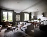Un salón rectangular amueblado con sofá gris, sillón marrón, mesa de centro y alfombra. Cocina abierta con mesa de comedor.