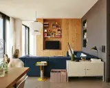 Un salón moderno con sofá azul, estanterías de madera y lámparas colgantes. Un espacio acogedor para **tini living**.