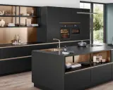 Elegantes cocinas pequeñas con isla central negra, gabinetes dorados y electrodomésticos integrados.