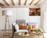 Ideas para decorar piso alquiler low cost: sofá gris, cojines coloridos, mesa auxiliar dorada, lámpara de pie y estantería con libros.