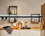 Cocinas sin muebles altos, con estantes flotantes y decoración minimalista. Encimera de madera con fregadero negro, jarrones y calabazas.