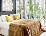 Cama acogedora con manta peluda, cojines amarillos y arte abstracto. Un diseño moderno para decorar habitación con luz natural.