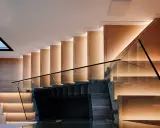 Moderna escalera de madera con iluminación indirecta y barandillas de cristal, vistas en el salón.