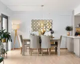Comedor elegante con mesa de madera y sillas tapizadas, sobre un suelo sisal. Decoración con espejos circulares y lámpara colgante.