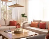 Salones pequeños con encanto: sofás beige, cojines terracota y naranja, mesa de madera, plantas y luz natural.