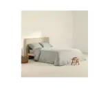 Cama con funda nordica 180x220 en tono gris claro, almohadas a juego y una cesta de mimbre al lado.