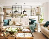 Salones con color: sofás beige, cojines turquesas y mantas suaves crean un ambiente acogedor. Una mesa de centro de madera con flores y libros completa la escena.