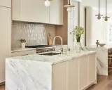 Elegante cocina atemporal con isla de mármol, gabinetes crema y electrodomésticos de acero inoxidable. Un jarrón con flores ilumina el espacio.