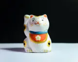 Maneki-neko blanco con detalles dorados y flor, ideal para feng shui en casa para la prosperidad.