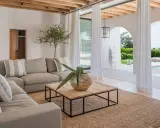 Sofá gris, mesa de centro de madera y alfombra de yute en un salón luminoso con vistas a una piscina.