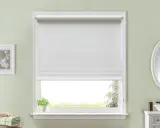 Persiana enrollable blanca que cubre la mayor parte de la ventana. Un pequeño paquete de toallas verdes y blancas descansa en la repisa.