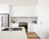 Cocinas blancas elegantes con encimeras de cuarzo, electrodomésticos de acero inoxidable y suelo de madera.