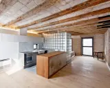 Cocina moderna con isla de madera y cristal, techos de vigas expuestas. Un espacio abierto que evoca la idea de como tirar un tabique para crear amplitud.