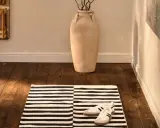 Alfombra pasillero a rayas blancas y negras, con zapatillas deportivas y un jarrón grande.