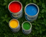 Latas de pintura para pintar plástico en rojo, azul, amarillo y verde, rodeadas de hojas verdes.