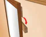 Detalle de cómo colgar un espejo: una pieza de madera se desliza sobre otra, indicando el método de fijación.