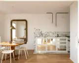 Comedores pequeños con encanto, con mesa redonda de madera, sillas blancas y un gran espejo dorado. La cocina integrada tiene encimera de mármol y armarios con puertas de espejo.