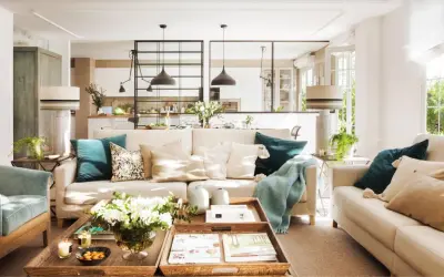 Salones con color: sofás beige, cojines turquesas y mantas suaves crean un ambiente acogedor. Una mesa de centro de madera con flores y libros completa la escena.