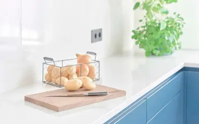 Encimeras de cocina blancas y lisas, con patatas y cebollas listas para cocinar.