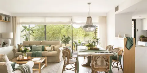 Elegante decoracion salon con sofás, mesa de comedor de madera, sillas de mimbre y gran ventanal con vistas al exterior.