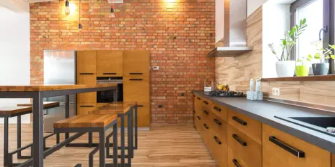 Cocina estilo industrial con paredes de ladrillo visto, muebles de madera y metal, y una isla con bancos.