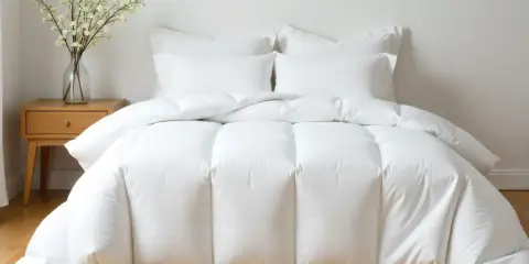 Cama impecable con edredón plumón oca blanco y cojines. Un jarrón con flores decora la mesita de noche.