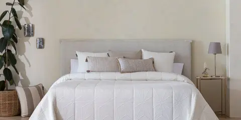 Una cama vestida con una colcha bouti beige de diseño geométrico, cojines y una planta decorativa.