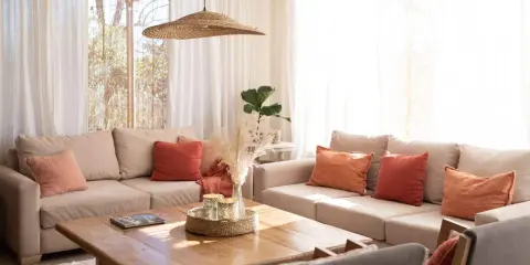 Salones pequeños con encanto: sofás beige, cojines terracota y naranja, mesa de madera, plantas y luz natural.