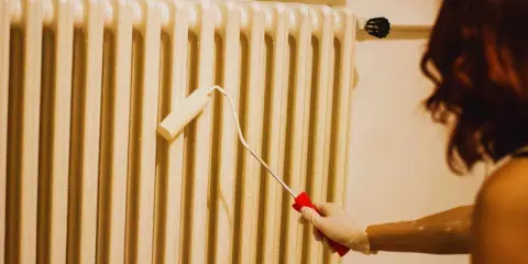 Persona con guantes blancos pinta un radiador con un rodillo.