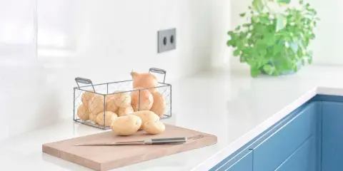 Encimeras de cocina blancas y lisas, con patatas y cebollas listas para cocinar.