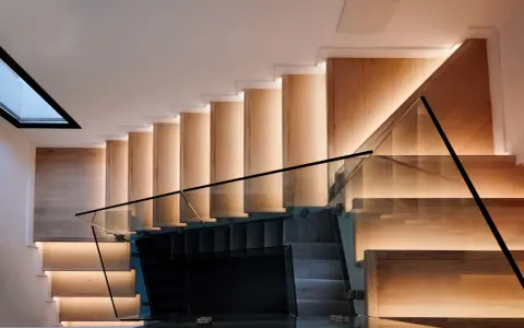 Moderna escalera de madera con iluminación indirecta y barandillas de cristal, vistas en el salón.