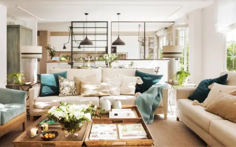 Salones con color: sofás beige, cojines turquesas y mantas suaves crean un ambiente acogedor. Una mesa de centro de madera con flores y libros completa la escena.