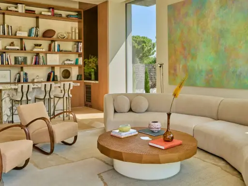 Sofá curvo y sillones de diseño contemporáneo, estanterías llenas de libros y arte abstracto en un salón luminoso.
