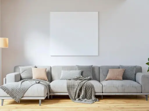 Un sofá gris moderno, listo para decorar con cojines y mantas, junto a una lámpara y una planta.
