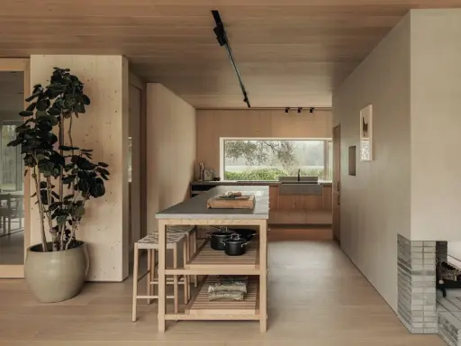 Un acogedor salón cocina pequeño con isla central, mucha madera y una gran ventana al exterior.