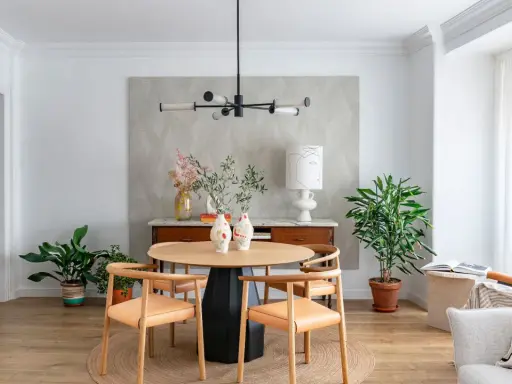 Comedor con mesa redonda de madera, sillas de cuero, lámpara moderna y plantas. Ideal para decorar piso moderno y elegante.