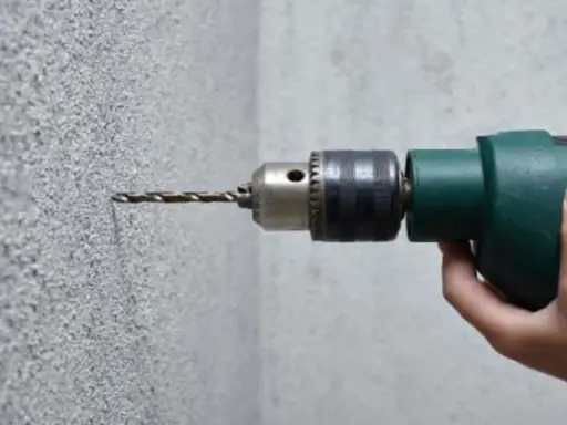 Taladrando hormigón con un taladro. La broca se adentra en la pared texturizada.