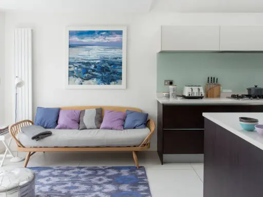 Acogedora cocina con un cómodo sofá de madera y cojines coloridos, junto a una isla y un cuadro de paisaje marino.