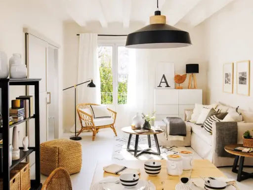 Acogedor salón estilo nórdico con sofá, sillón de mimbre, mesa de centro y estantería negra.
