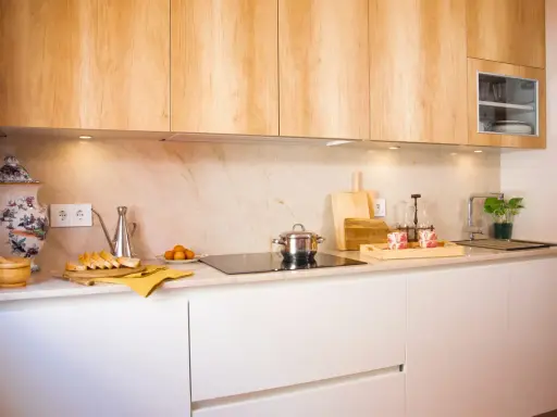 Cocina blanca y madera con encimera de mármol. Hay pan, huevos, una olla y una planta.