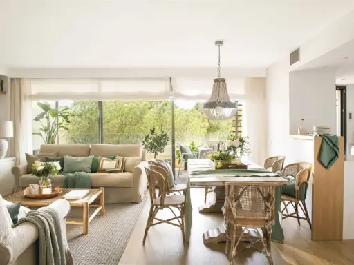 Elegante decoracion salon con sofás, mesa de comedor de madera, sillas de mimbre y gran ventanal con vistas al exterior.