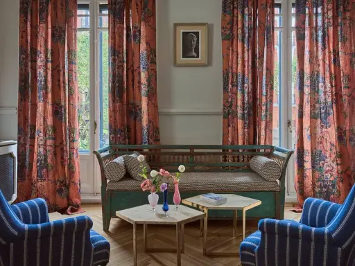 Cortinas de lino estampado con motivos florales y botánicos en tonos anaranjados, complementando un sofá vintage y sillones a rayas.