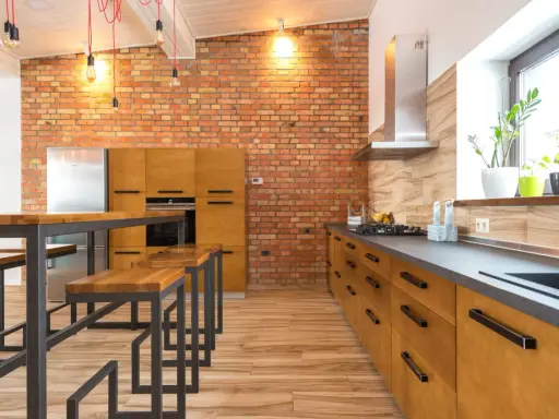 Cocina estilo industrial con paredes de ladrillo visto, muebles de madera y metal, y una isla con bancos.