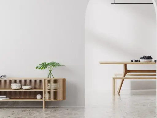 Un espacio minimalista con un aparador de madera y un comedor. Las paredes lisas y el suelo pulido crean un ambiente sereno.