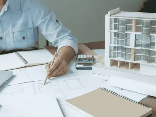 Una arquitecta de interiores dibuja planos junto a una maqueta de edificio.
