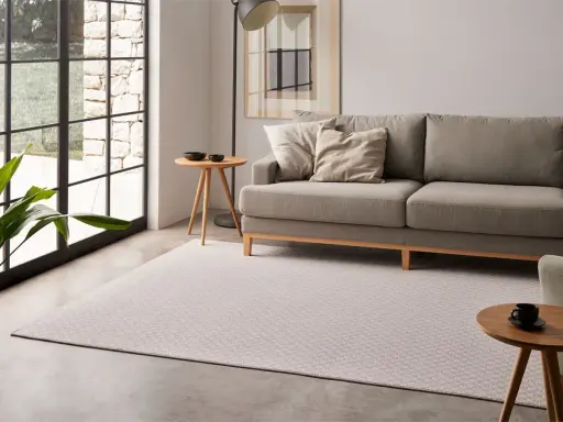 Elegante salón con sofá gris y alfombra de patrones geométricos, mostrando diversos tipos de alfombras para un hogar acogedor.