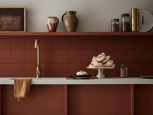 Encimera de cocina pintada en tono terracota, con grifería dorada y detalles decorativos.