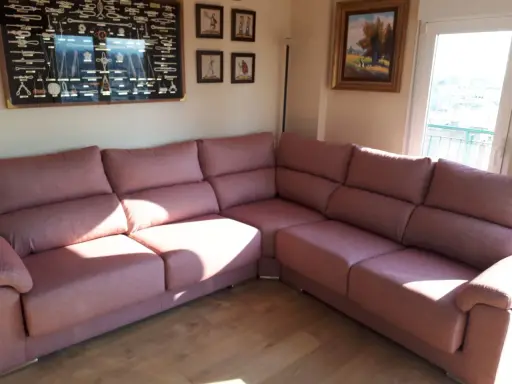Cómodo sofá rinconera rosa, ideal para decorar salón. En la pared, un cuadro de nudos marineros y pinturas.
