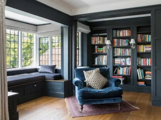 Acogedor rincón lectura salón con sillón azul, ventana con banco y estanterías llenas de libros.