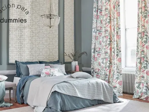 Cama elegante con ropa de cama azul y cojines florales, cortinas de proteas y papel tapiz geométrico. Un kilim Maimana aportaría calidez a este espacio.